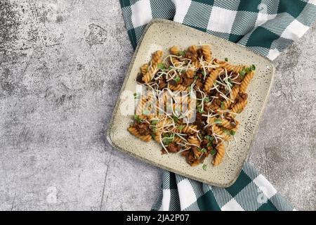 Auberginen- und Fleischpasta mit Kräutern auf einem quadratischen Teller auf dunklem Grund. Draufsicht, flach liegend` Stockfoto